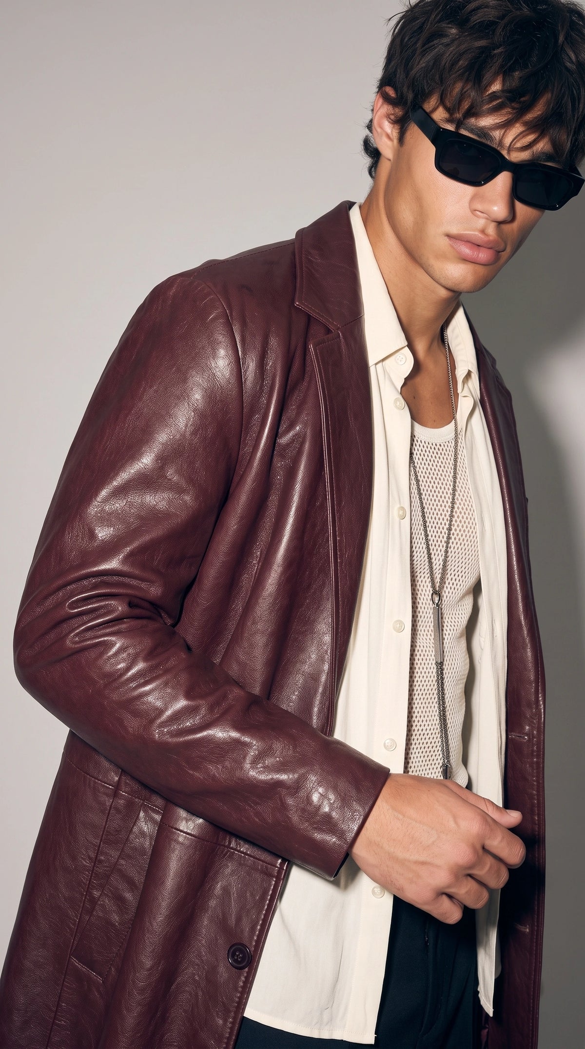 Close-up of a dark oxblood burgundy genuine leather coat highlighting its naturally textured surface, sharply defined notch lapels, chest welt pocket and carefully stitched leather panels. Subtle highlights across the deep wine-red finish bring out the material’s character, while the tailored construction gives this men’s statement overcoat a sophisticated designer-inspired appearance.