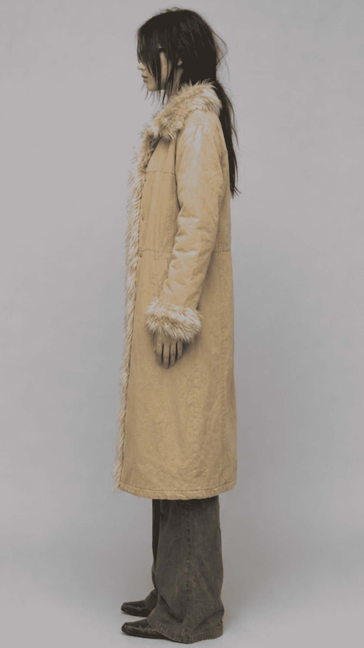 A model wearing a pastel yellow textured cotton long-coat, a black top, and cream wide-leg trousers, standing against a light gray studio background.