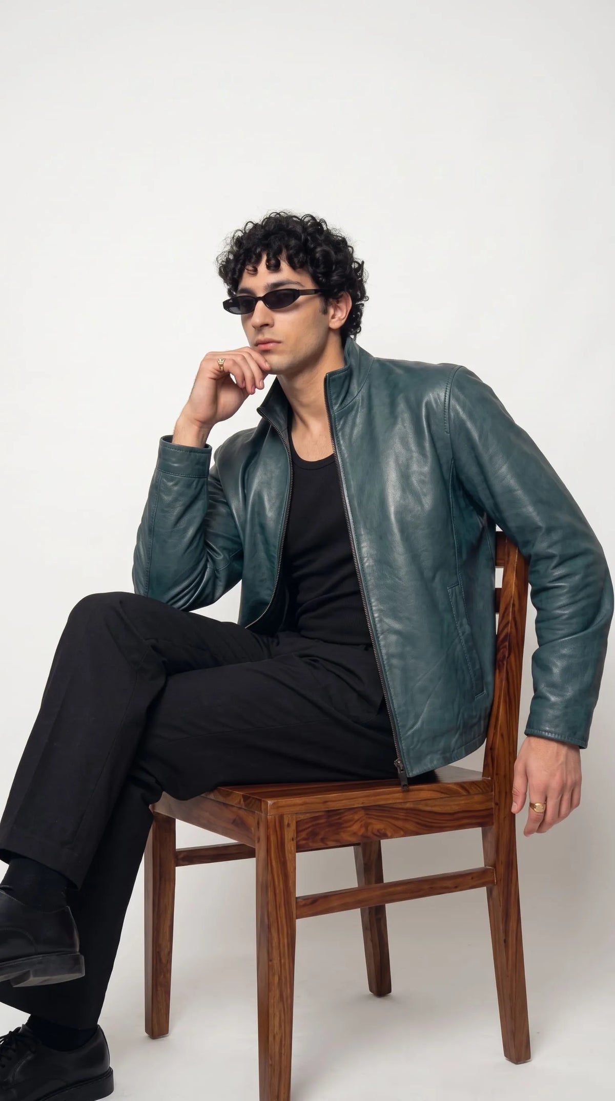 Petrol teal leather jacket with a streamlined band collar, fitted sleeves, subtle panel stitching and a full-length silver-tone zipper, paired with a black sleeveless top and dark trousers for a modern designer-inspired urban outfit.