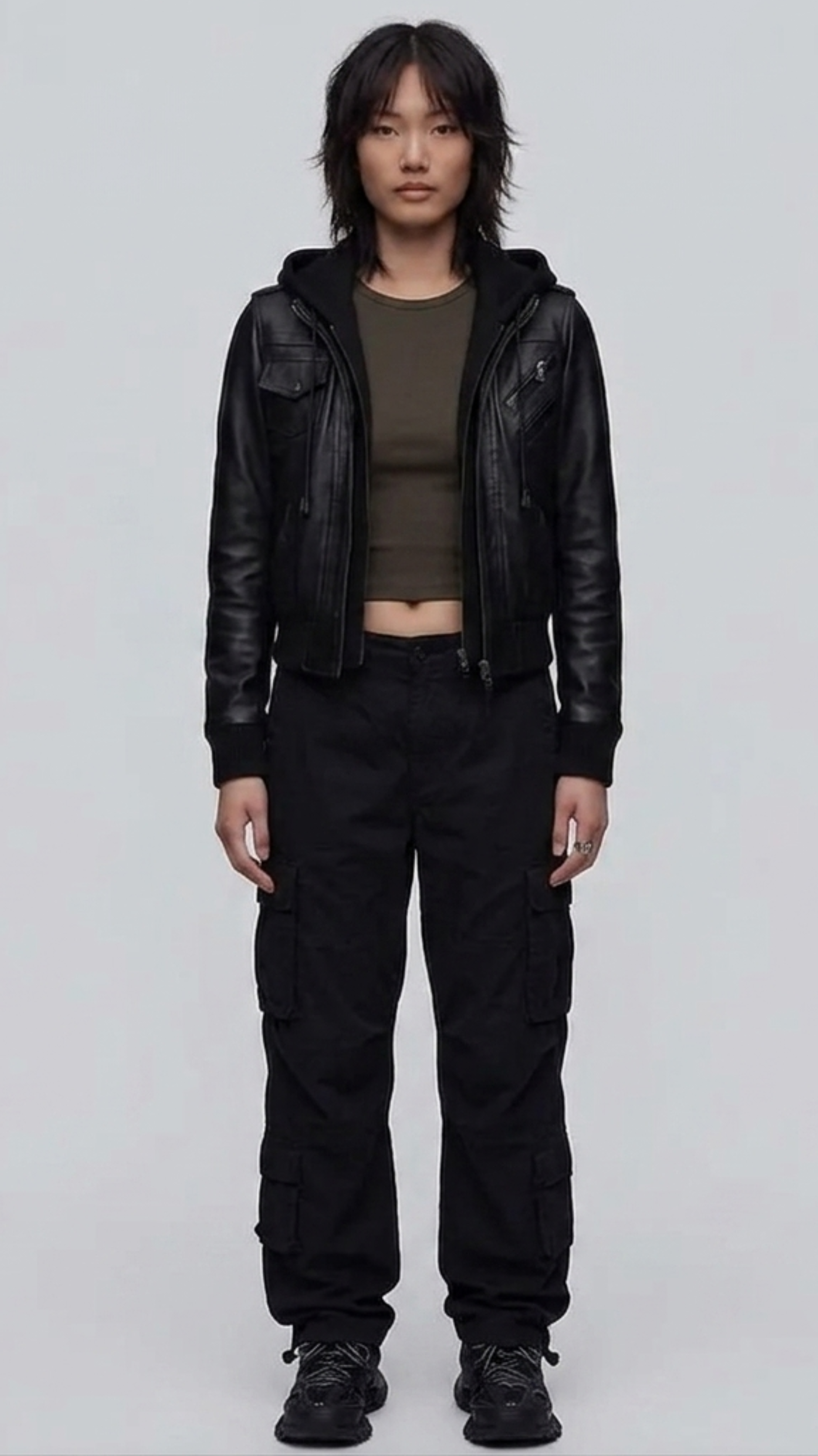 Front view lookbook photography of a model showcasing the Jackero premium black leather hooded Y2K bomber jacket styled with modern urban techwear.