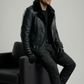 Man in a black leather jacket sitting on a gray chair against a plain background