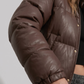 Minimalist lookbook style photography of a stylish chocolate brown winter puffer coat on a clean neutral backdrop.