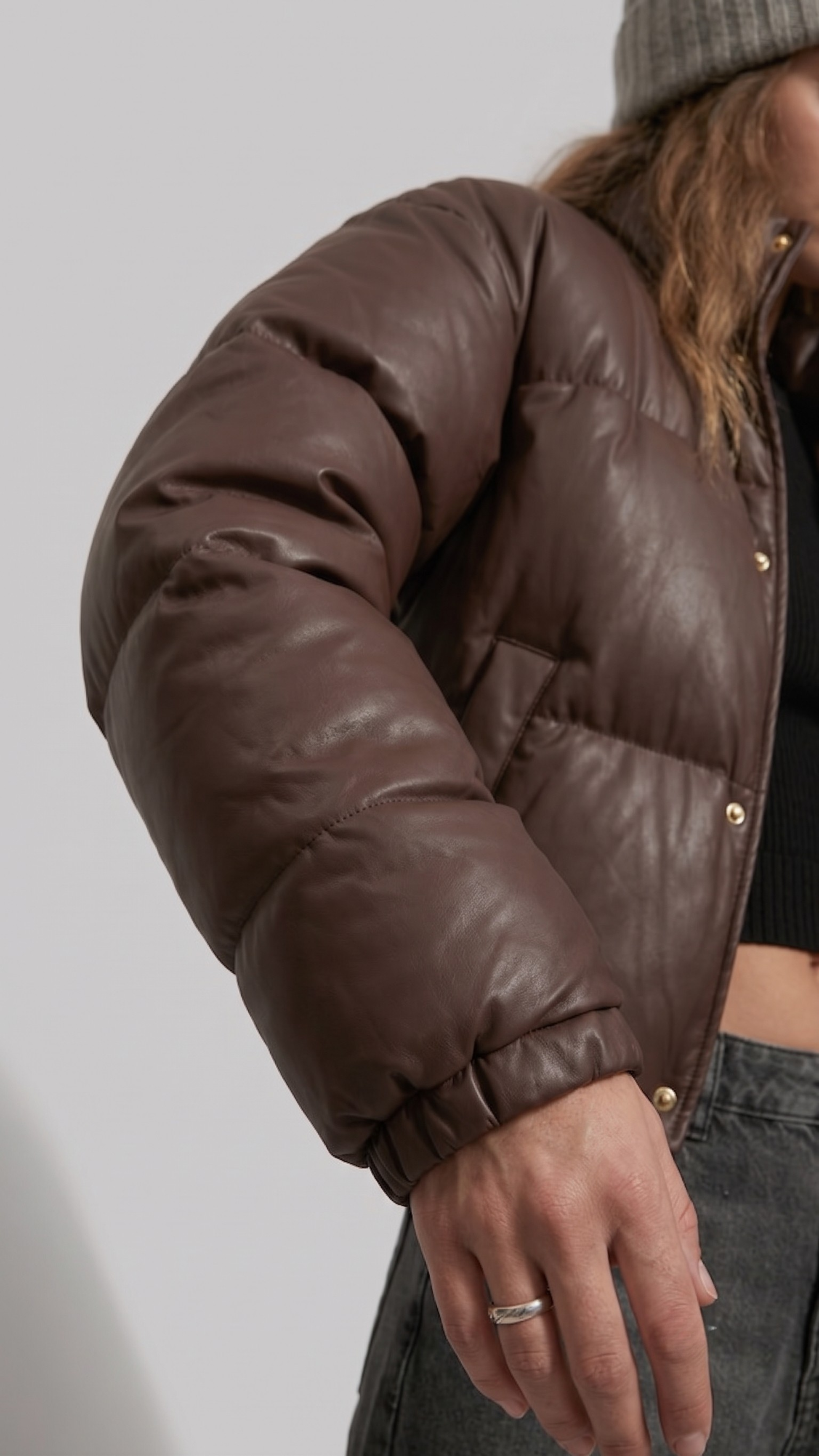 Minimalist lookbook style photography of a stylish chocolate brown winter puffer coat on a clean neutral backdrop.
