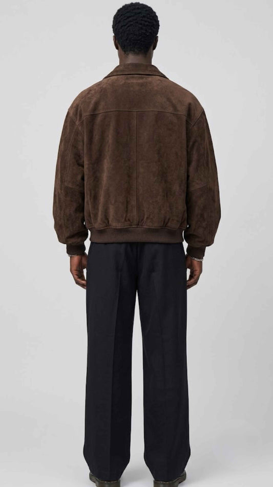 A model shown from the back wearing a jackero brown suede jacket and black wide-leg trousers against a light gray studio background.