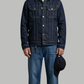 Man wearing a denim jacket and jeans holding a cap on a gray background