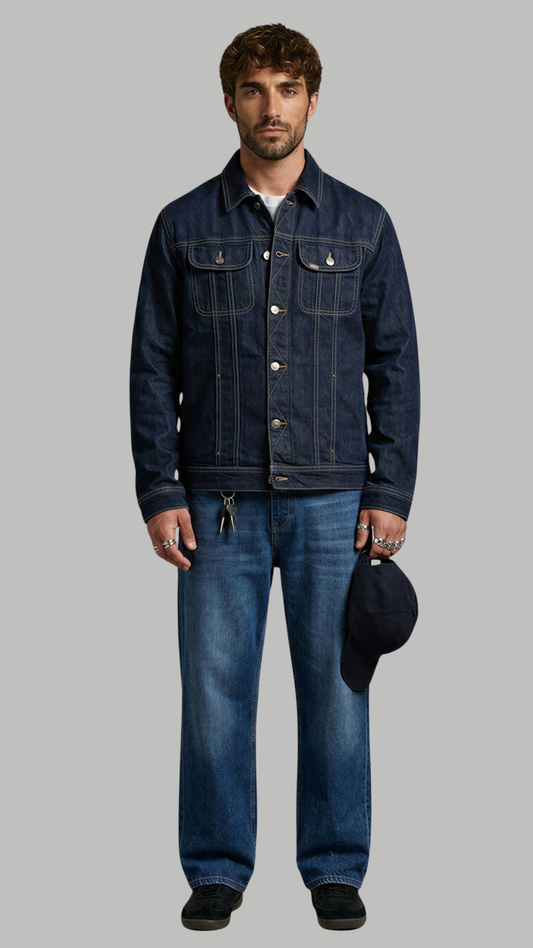 Man wearing a denim jacket and jeans holding a cap on a gray background