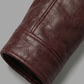 A close-up of a dark burgundy leather sleeve or cuff, showing the textured grain and stitching, set against a solid gray background.