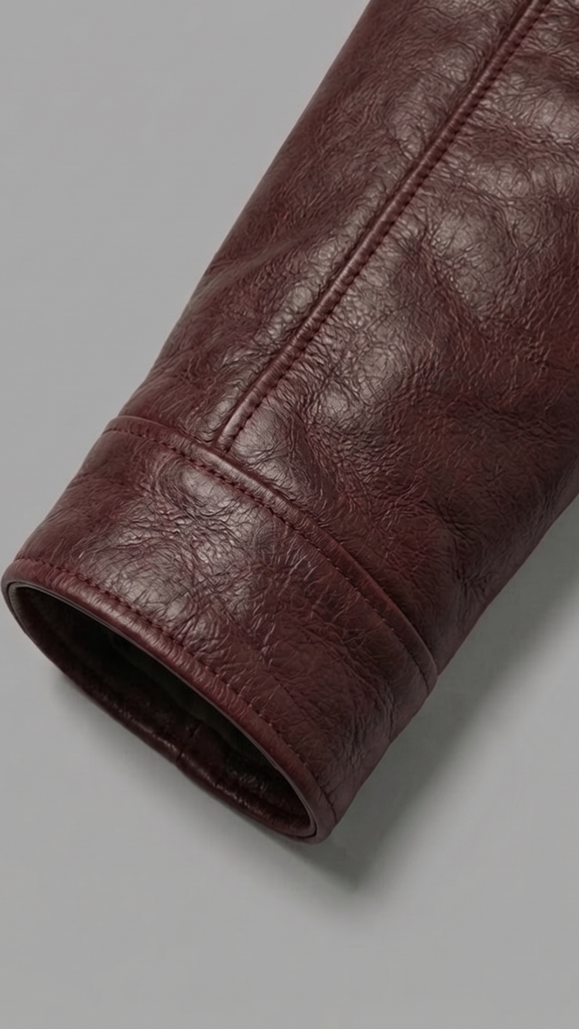A close-up of a dark burgundy leather sleeve or cuff, showing the textured grain and stitching, set against a solid gray background.
