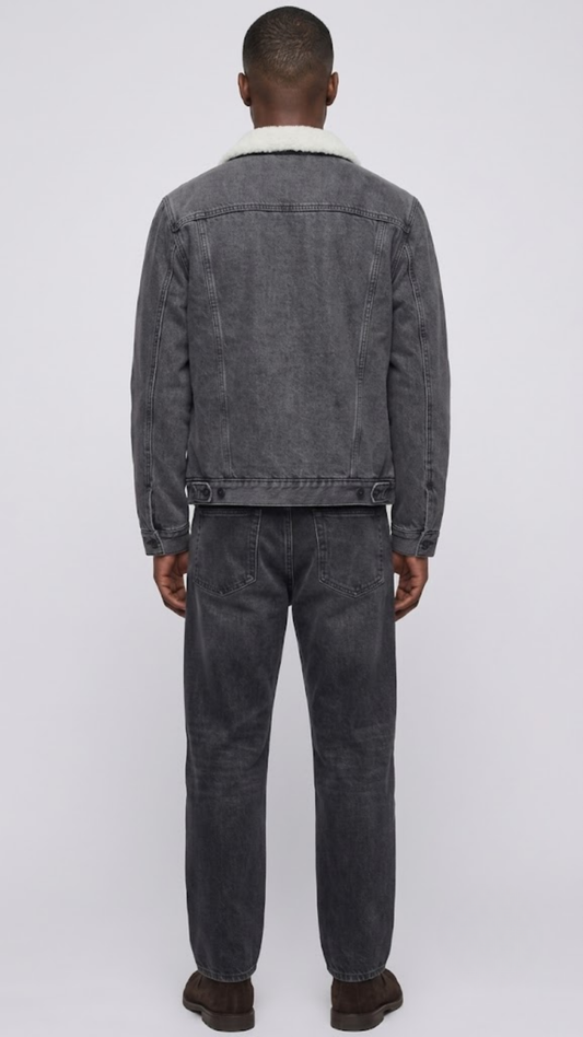 A model shown from the back wearing a washed charcoal denim jacket with white shearling and against a neutral gray background.