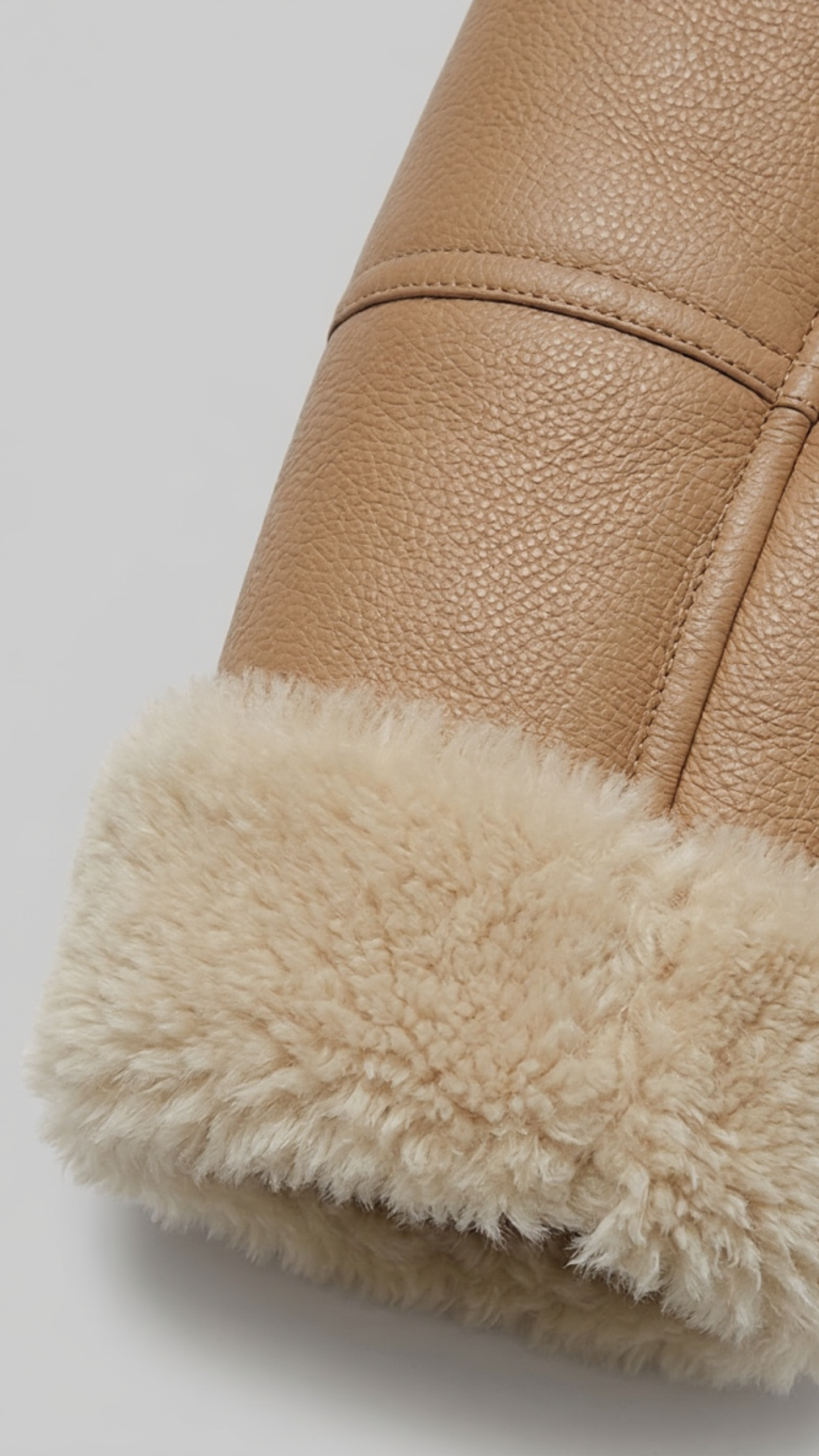 Close-up of a light beige leather jacket with soft cream fur lining on a light gray background