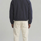 Symmetrical back view of the dark navy cotton coach jacket showing the clean minimalist drape and straight hem construction on a solid grey backdrop.