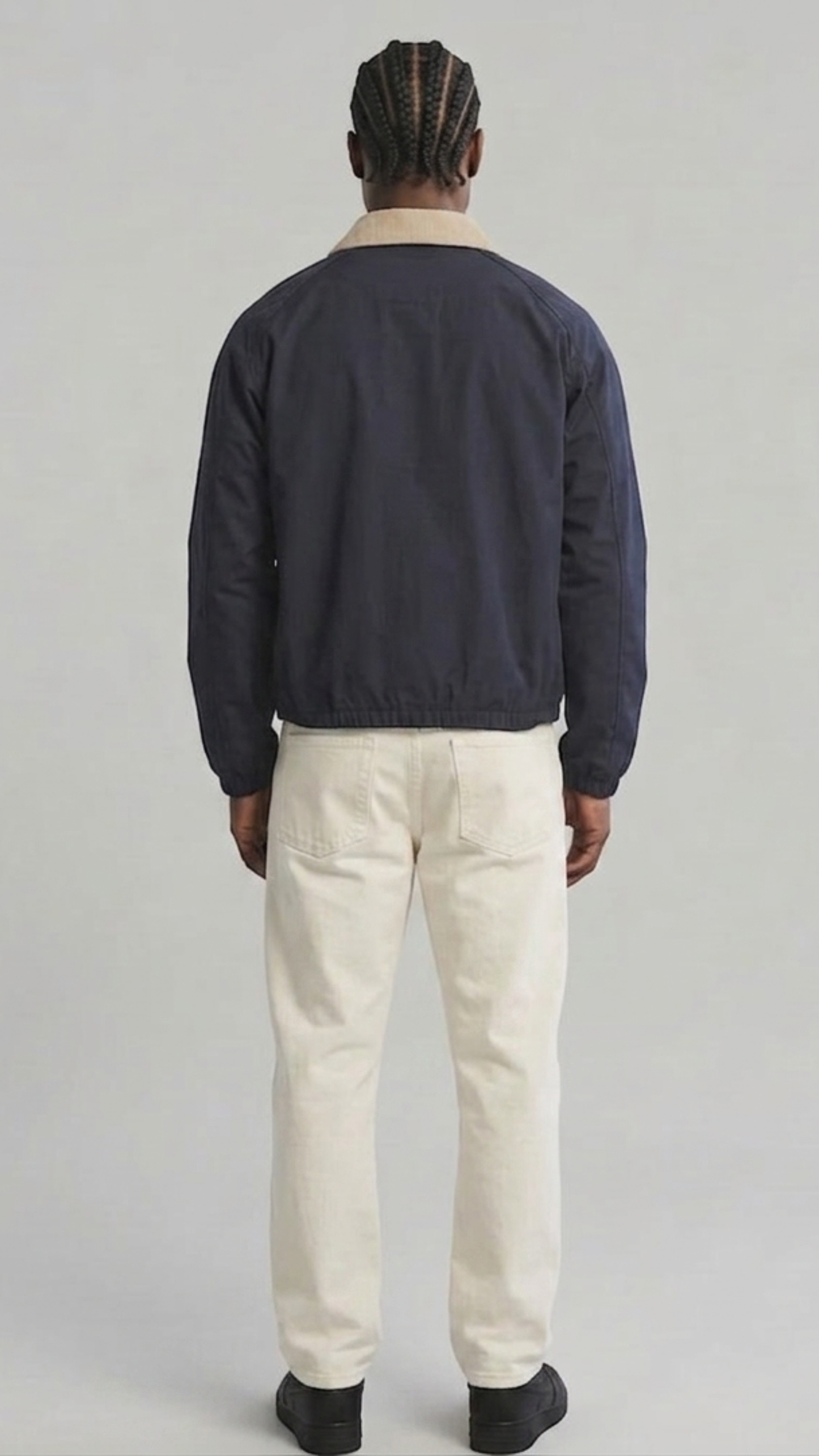 Symmetrical back view of the dark navy cotton coach jacket showing the clean minimalist drape and straight hem construction on a solid grey backdrop.