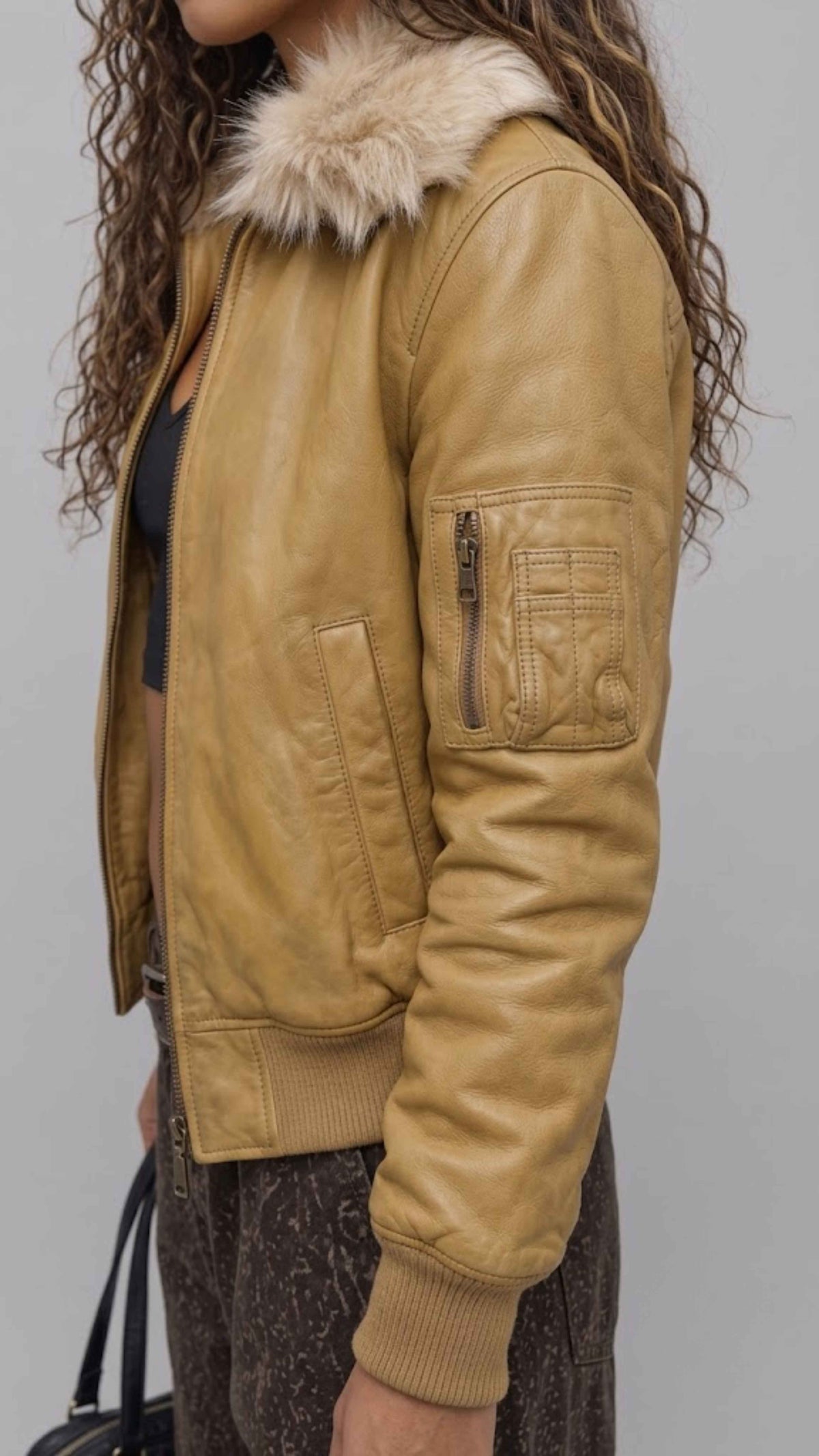 Macro close-up of heavy-duty metal zipper pulls and side slash pockets on dark mustard leather outerwear