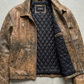 Brown leather jacket with quilted black lining on a gray surface