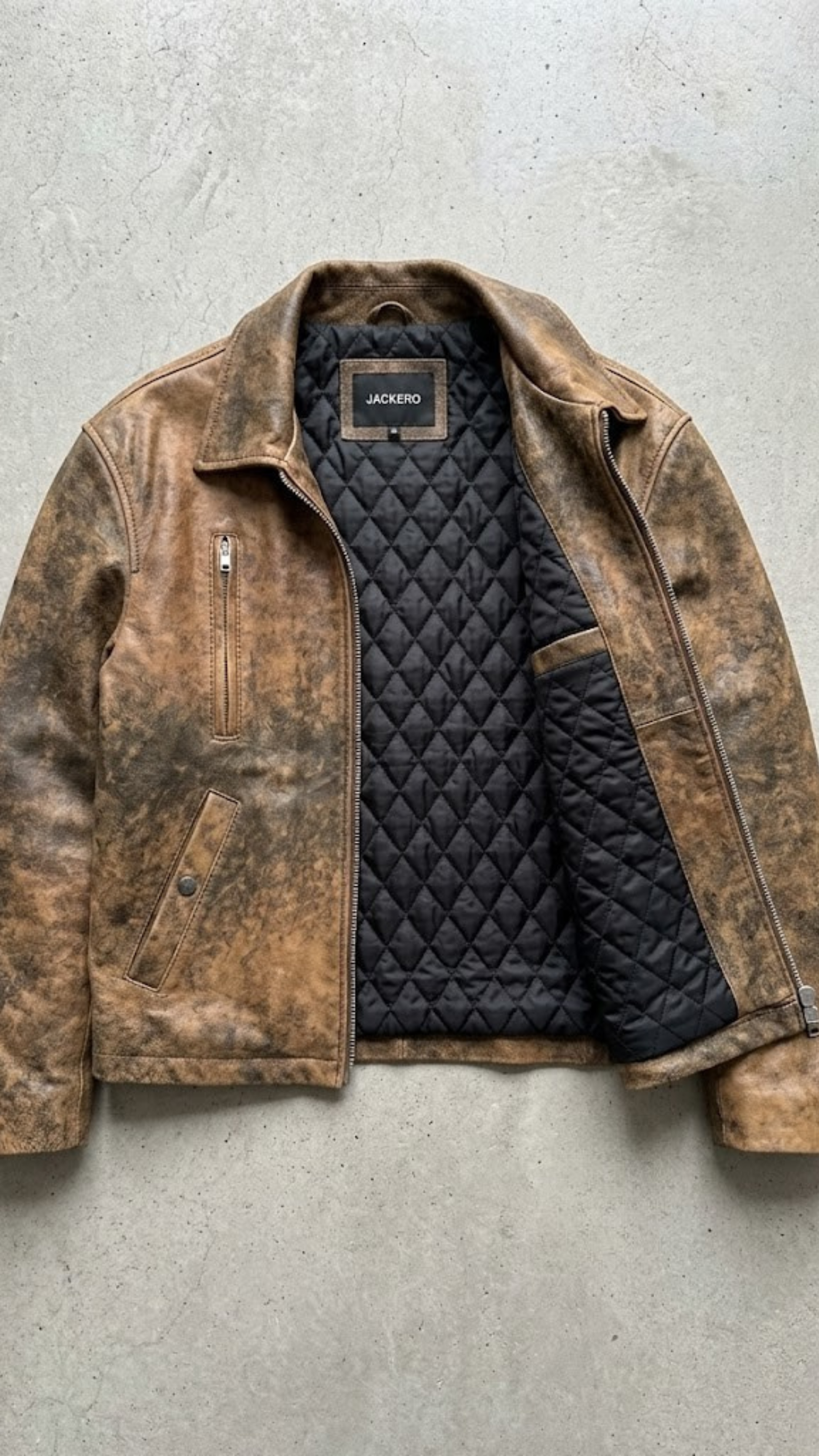 Brown leather jacket with quilted black lining on a gray surface