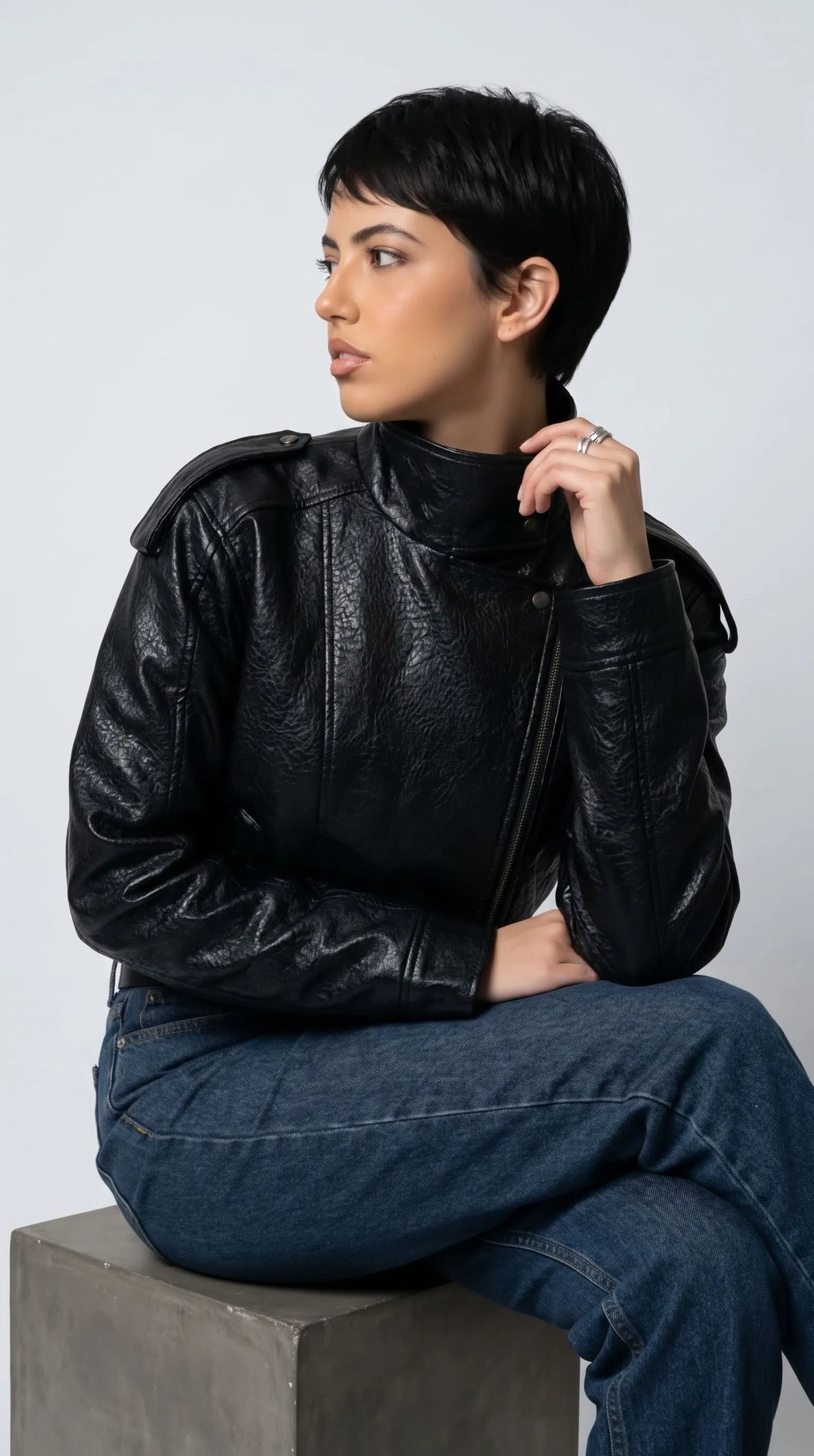 Modern streetwear styling featuring a baggy black textured leather jacket with an architectural high collar, structured shoulder tabs and a clean oversized silhouette, paired with denim for effortless everyday edge.