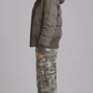 Side angle of model styled in a relaxed oversized olive puffer coat showing wide drop shoulders and deep side pockets