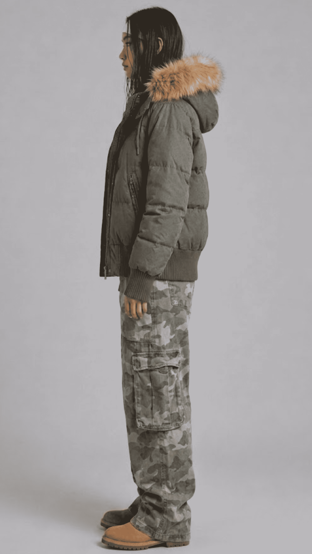 Side angle of model styled in a relaxed oversized olive puffer coat showing wide drop shoulders and deep side pockets