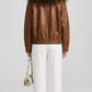 Minimalist studio portrait showcasing a women's oversized caramel brown lambskin leather coat.