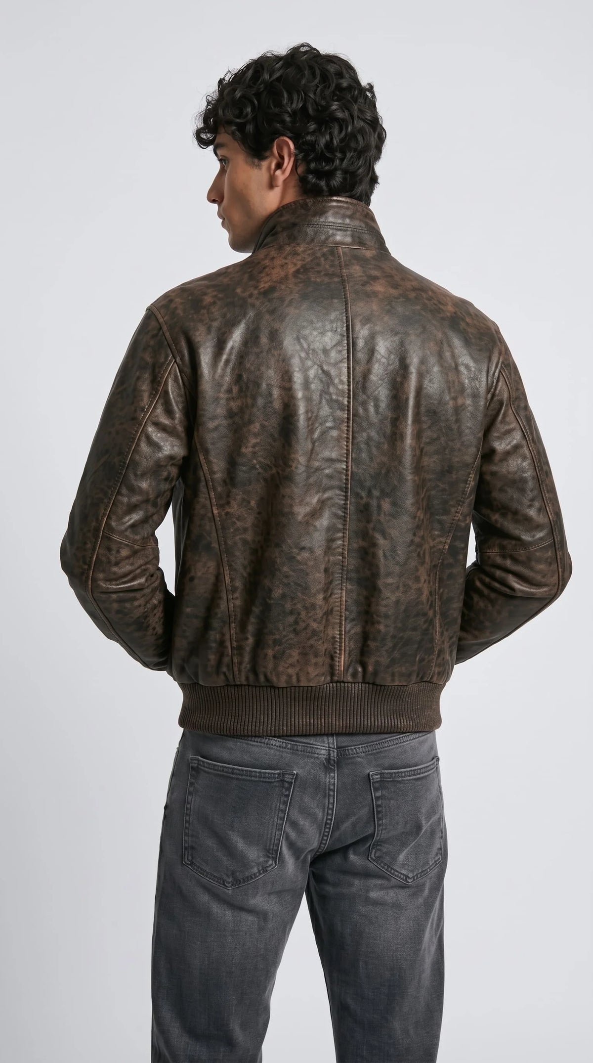 Retro 90s style brown leather bomber jacket for men with rustic worn-in look and elastic ribbed cuffs, arms crossed pose