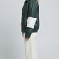 the minimalist collar construction and sporty shoulder paneling of a dark green striped leather jacket.