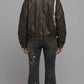 A model shown from the back wearing a dark brown leather jacket with a brown fur collar, paired with dark gray flared jeans featuring floral embroidery down the back.