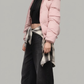 Streetwear style showcasing a designer oversized pastel pink puffer jacket with a fur hood and dark grey wide-leg trousers.