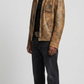 A man modeling a distressed brown leather jacket with a tan and black mottled pattern, worn over a black shirt and dark jeans, against a light gray studio background.