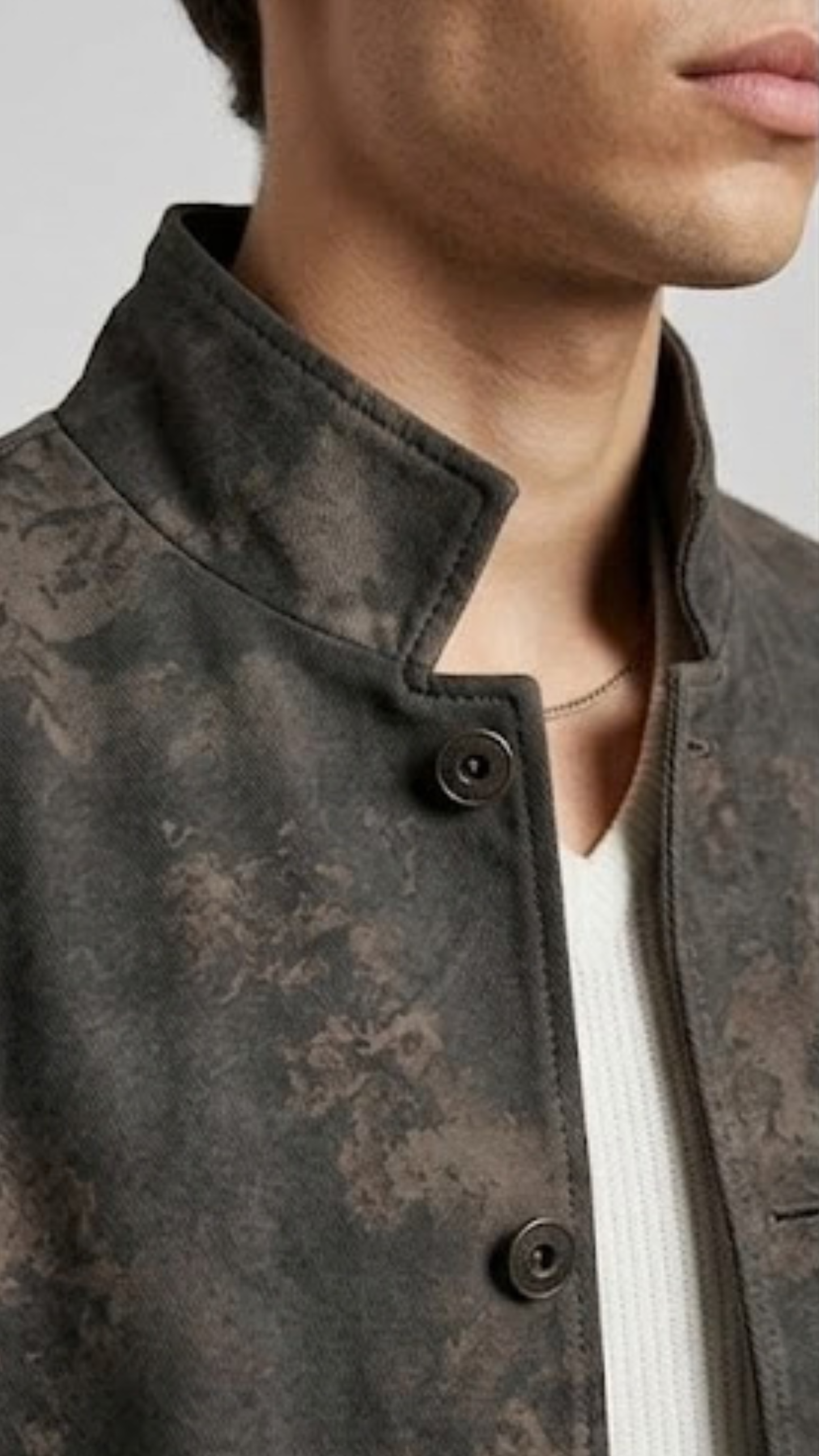Close-up of a person wearing a textured charcoal distressed leather jacket with a neutral background