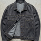 A washed dark charcoal denim jacket, laid flat on a gray concrete surface.