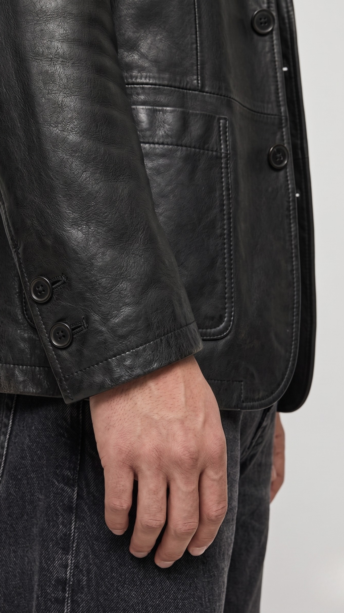 Close-up shot highlighting the seamless pocket stitching and premium button craftsmanship on a minimalist black leather suit jacket.