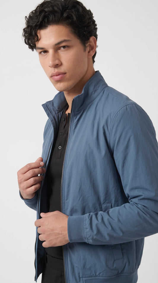 Close-up of a steel-cyan silk-cotton bomber jacket highlighting its smooth lightly lustrous fabric, neatly constructed stand-up collar and full-length metal zipper. The subtle blue-grey colour and clean front finish create a sophisticated minimalist look, making this men’s zip-up jacket an appealing choice for understated designer-inspired fashion and elevated casual outfits.