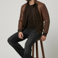Detailed studio shot highlighting the minimalist band collar, neat stitching, and metallic zipper accents of a dark brown suede jacket.