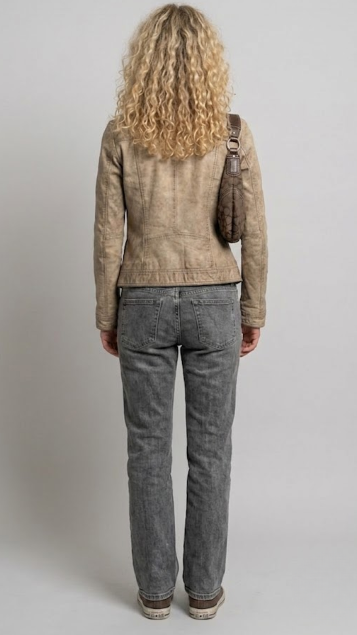 A model shown from the back wearing a cropped burgundy leather jacket with cream stripes on the shoulders and sleeves, paired with dark blue wide-leg jeans and white sneakers, against a solid gray background.