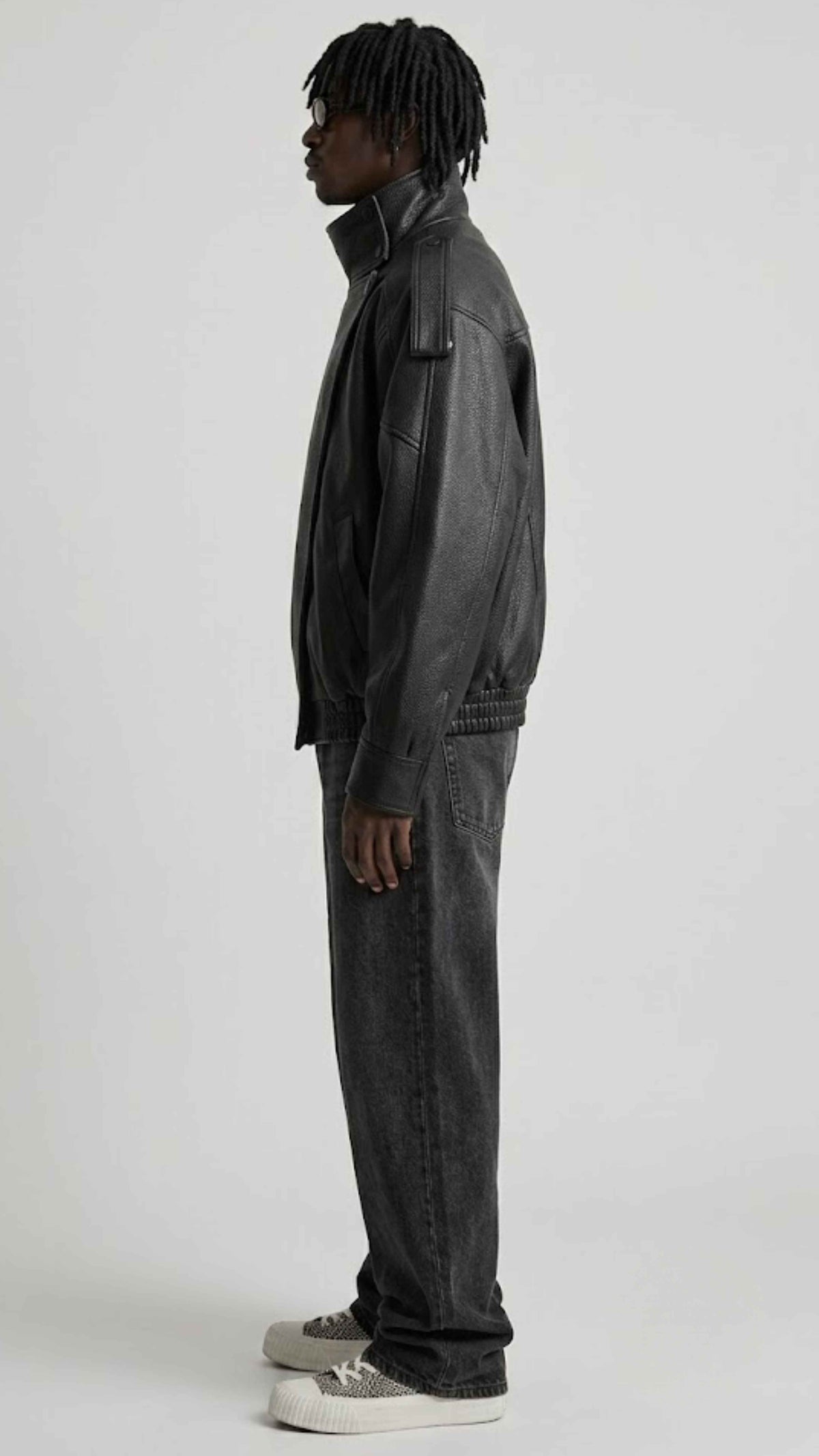 Side angle view showing waist slash pockets and structured panel stitching on loose fit black leather jacket.