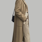 Woman wearing a beige coat and pants with a black handbag on a gray background