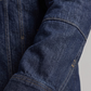 Close-up of a person wearing a dark blue denim jacket with rolled-up sleeve on a gray background