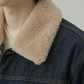 Close-up of a person wearing a dark indigo denim jacket with a thick beige sherpa fleece collar over a cream ribbed sweater.