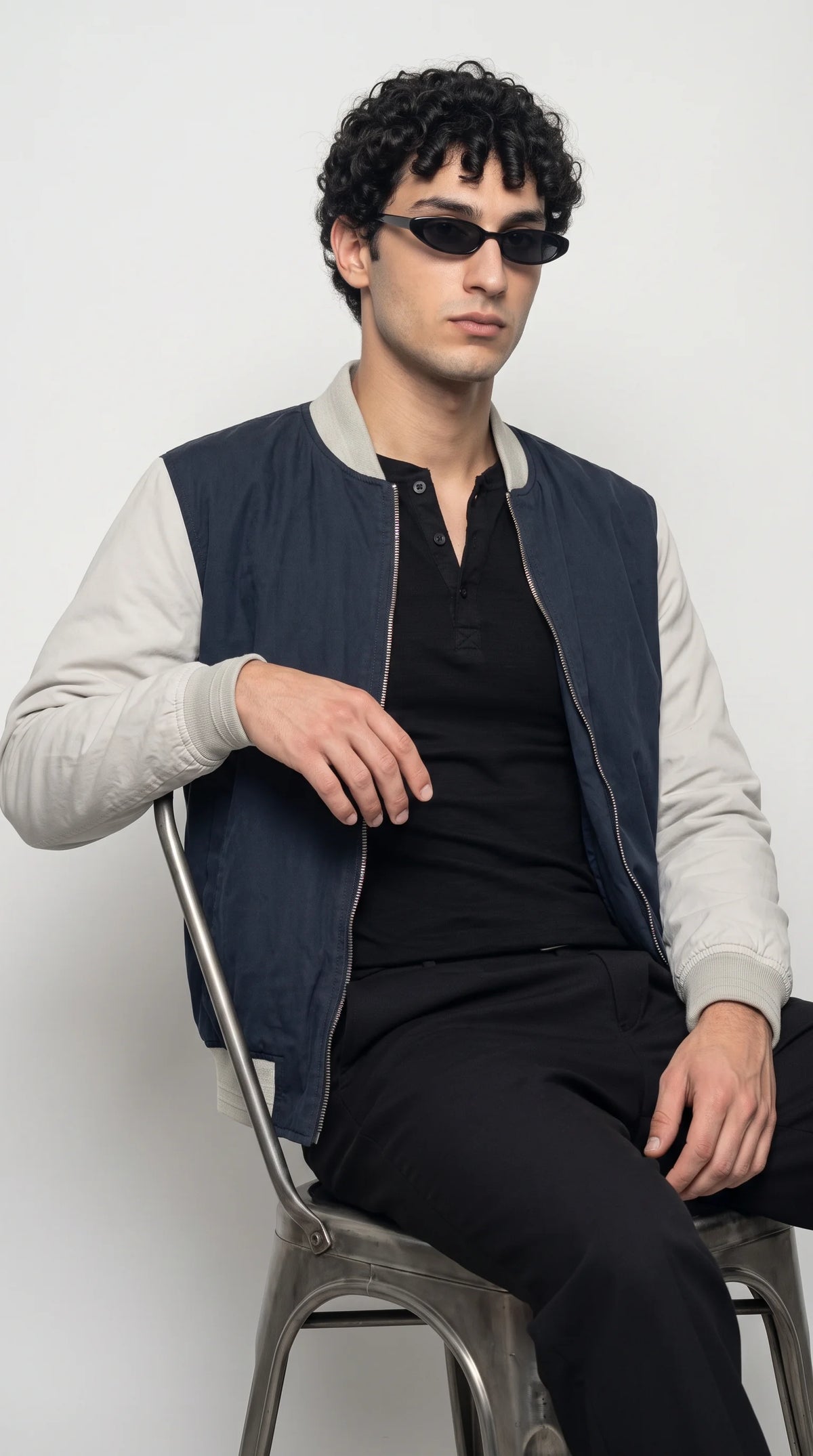 Two-tone navy and grey cotton bomber jacket styled with a black shirt and matching dark trousers, highlighting the light-grey sleeves, clean navy body, ribbed cuffs and streamlined zip-front design for understated everyday fashion and relaxed studio styling.