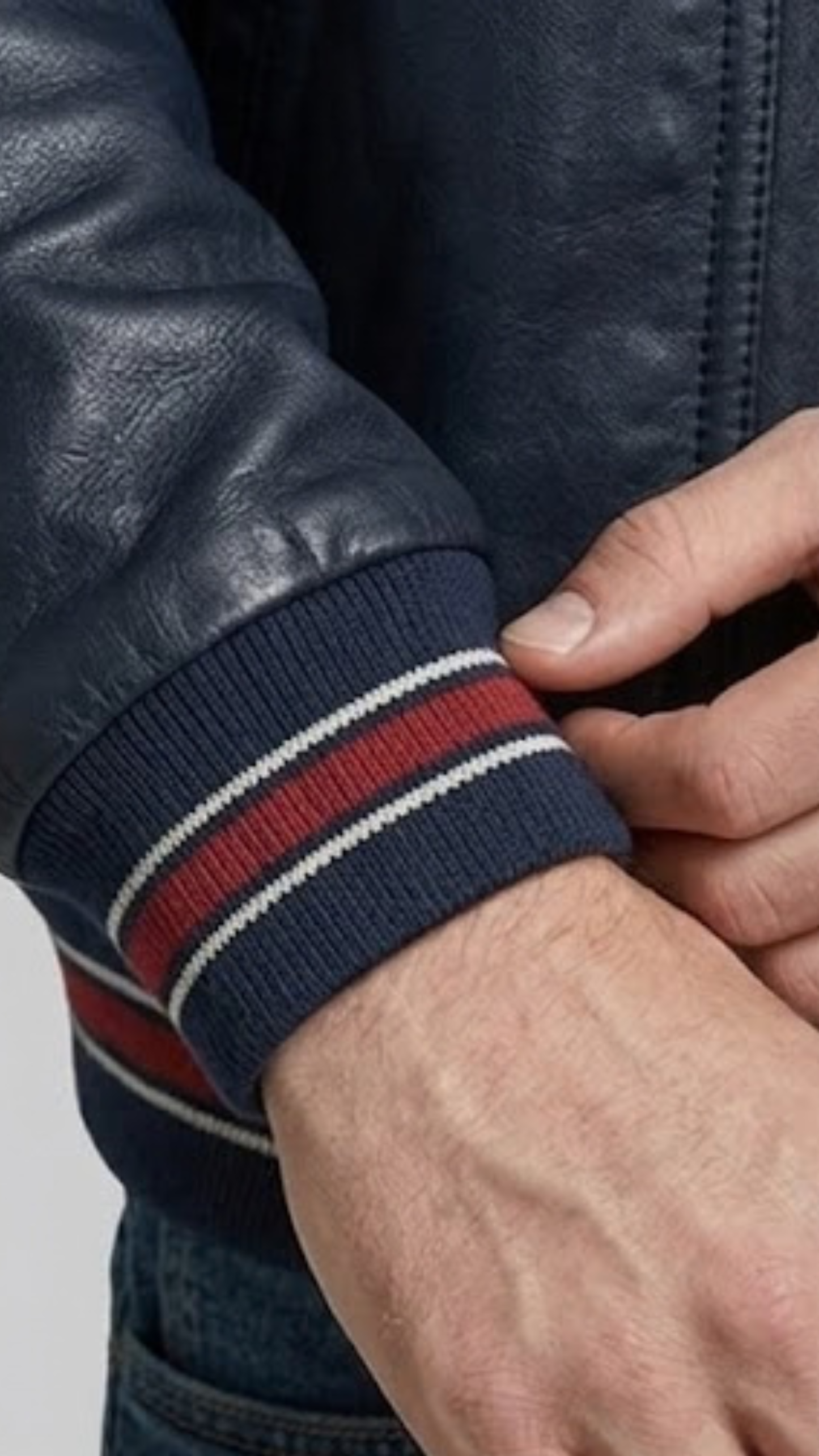 Close-up of a person wearing a dark blue jacket with a striped sleeve cuff.