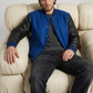 Men's contemporary high-fashion presentation featuring a classic blue and black letterman jacket styled for an edgy urban look.