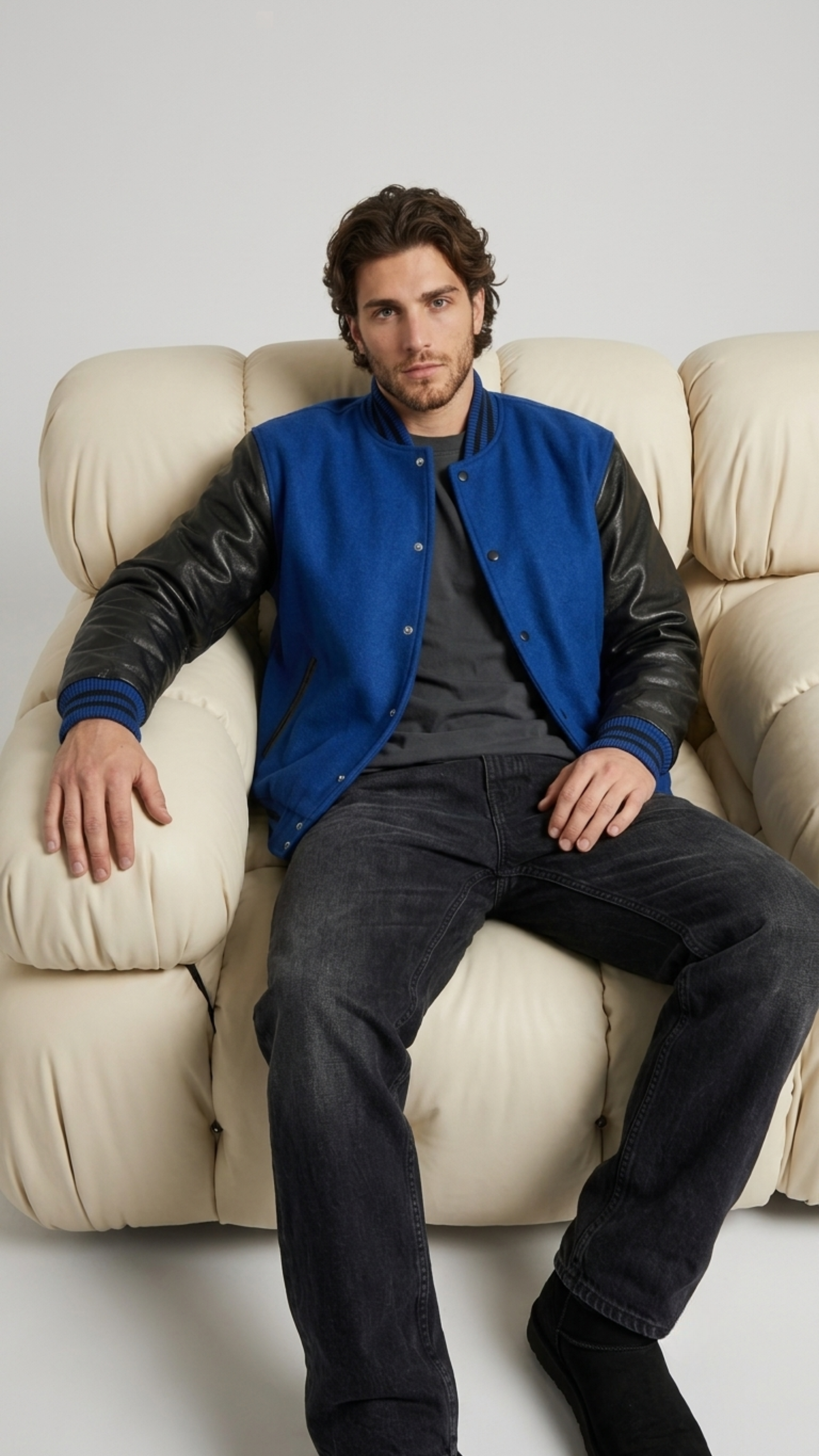 Men's contemporary high-fashion presentation featuring a classic blue and black letterman jacket styled for an edgy urban look.