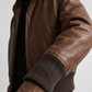 Macro detailed focus capture displaying the soft premium texture and deep dark cocoa tone of the genuine leather bomber jacket fabric.