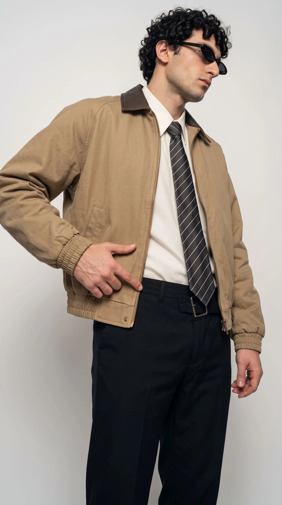Layered menswear outfit idea zip-up jacket worn over a cream collared shirt and black-and-white striped silk tie
