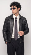 Men’s vintage-washed black genuine leather field jacket featuring a classic fold-down collar, full-length front zipper and practical utility pockets, styled with a crisp white shirt, striped tie and tailored black trousers for a refined smart-streetwear look.