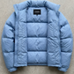 Close-up shot of a modern light blue puffer jacket highlighting the durable water-resistant fabric and premium zipper closure.