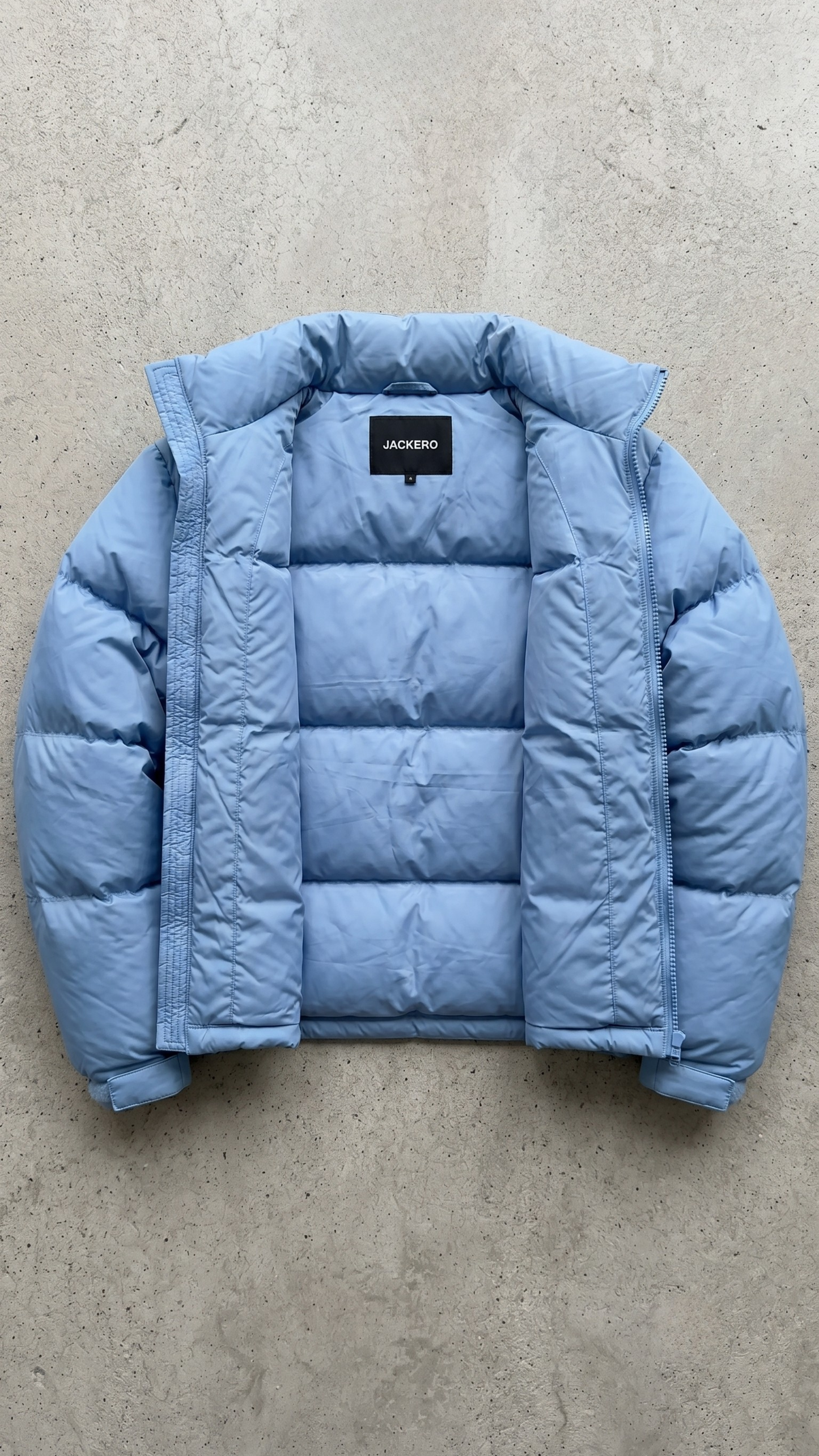 Close-up shot of a modern light blue puffer jacket highlighting the durable water-resistant fabric and premium zipper closure.