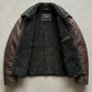 detail highlighting the dark brown leather panels paired with thick, soft black shearling on the lapels Two tone flight jacket flat-lay shot.