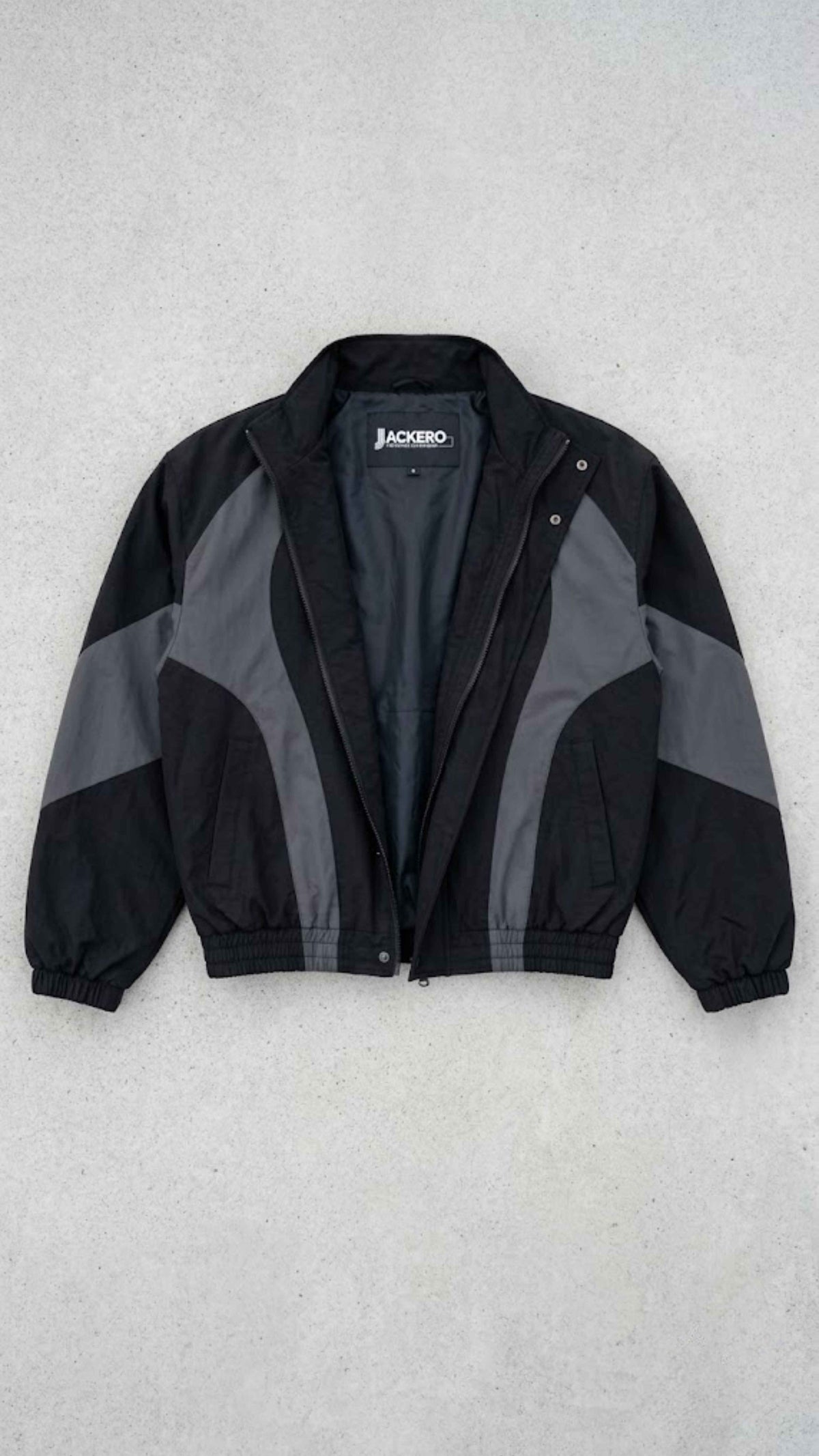 Flat lay presentation of Jackero black and dark grey oversized Y2K nylon jacket displaying internal lining and neck label