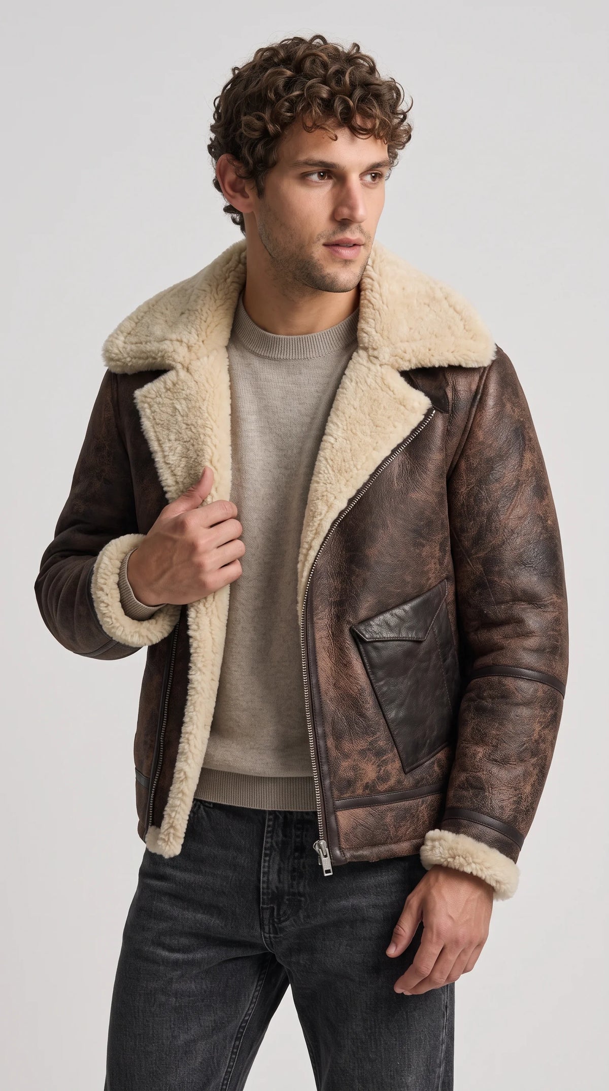 Dark espresso-brown distressed genuine leather aviator jacket with an oversized cream faux-shearling collar, exposed plush front trim and cuffs, an asymmetrical silver zipper and rugged weathered finish, styled with neutral knitwear for elevated winter streetwear.